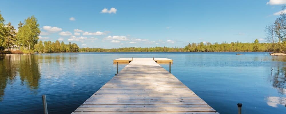 Bilden visar en brygga som går ut i en sjö med lugnt vatten. Blå himmel i bakgrunden.