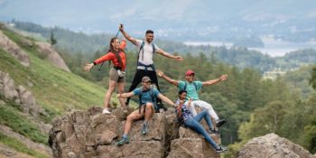 Bilden visar en grupp ungdomar, på en bergstopp, som slår ut med armarna och ser lyckliga ut