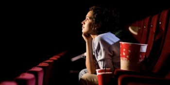 Bilden visar en person som sitter ensam i biosalong och tittar mot duken